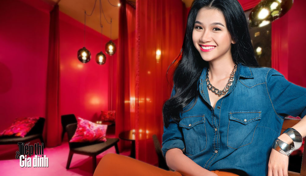 Thảo Nhi mặc áo jeans xanh, quần cam ngồi trong quán cà-phê màu đỏ